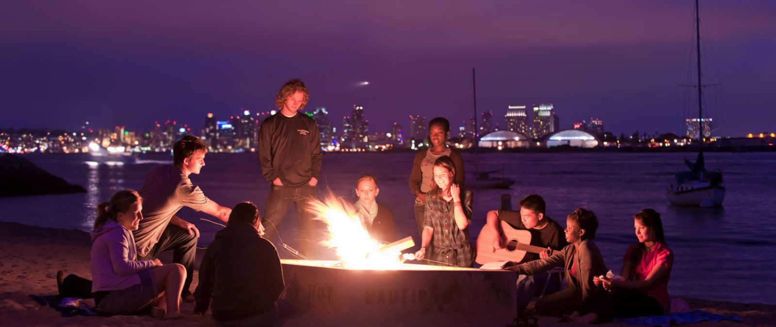 鶹 students have a beach bonfire at night and play music while at Shelter Island in San Diego.